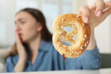 Photo of Shocked young woman holding pretzel with cockroach at white table indoors, selective focus. Pest problem