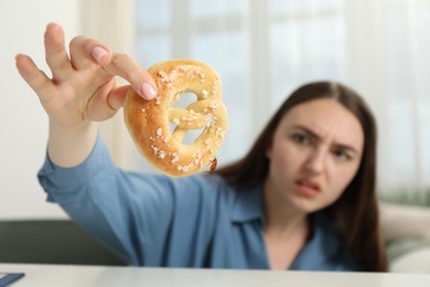 Photo of Shocked young woman holding pretzel with cockroach at white table indoors, selective focus. Pest problem
