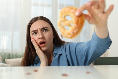 Photo of Shocked young woman holding pretzel with cockroach at white table indoors, selective focus. Pest problem