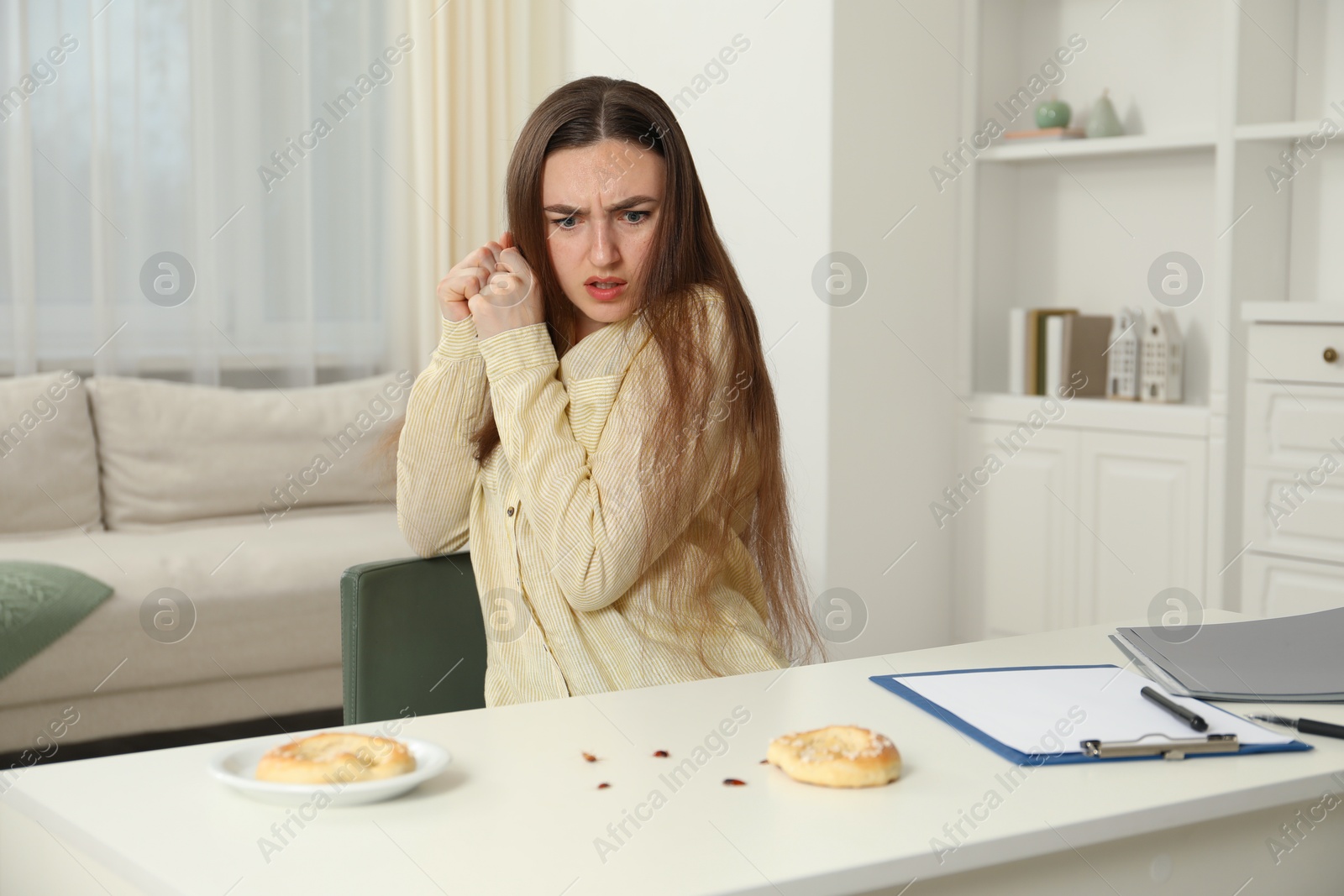 Photo of Emotional young woman looking in disgust at cockroaches at white table indoors. Pest problem