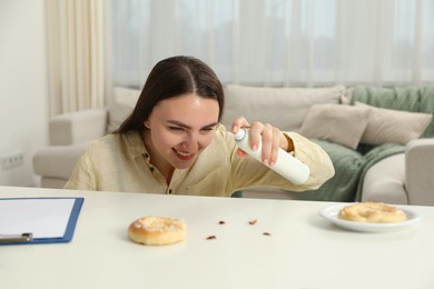 Photo of Emotional young woman spraying insecticide onto cockroaches at white table indoors. Pest problem