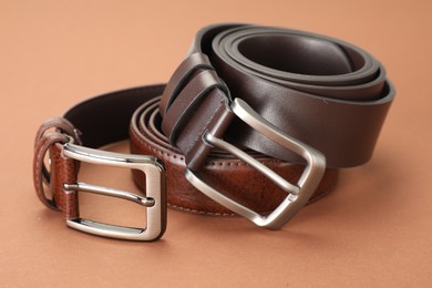 Photo of Two leather belts on pale brown background, closeup