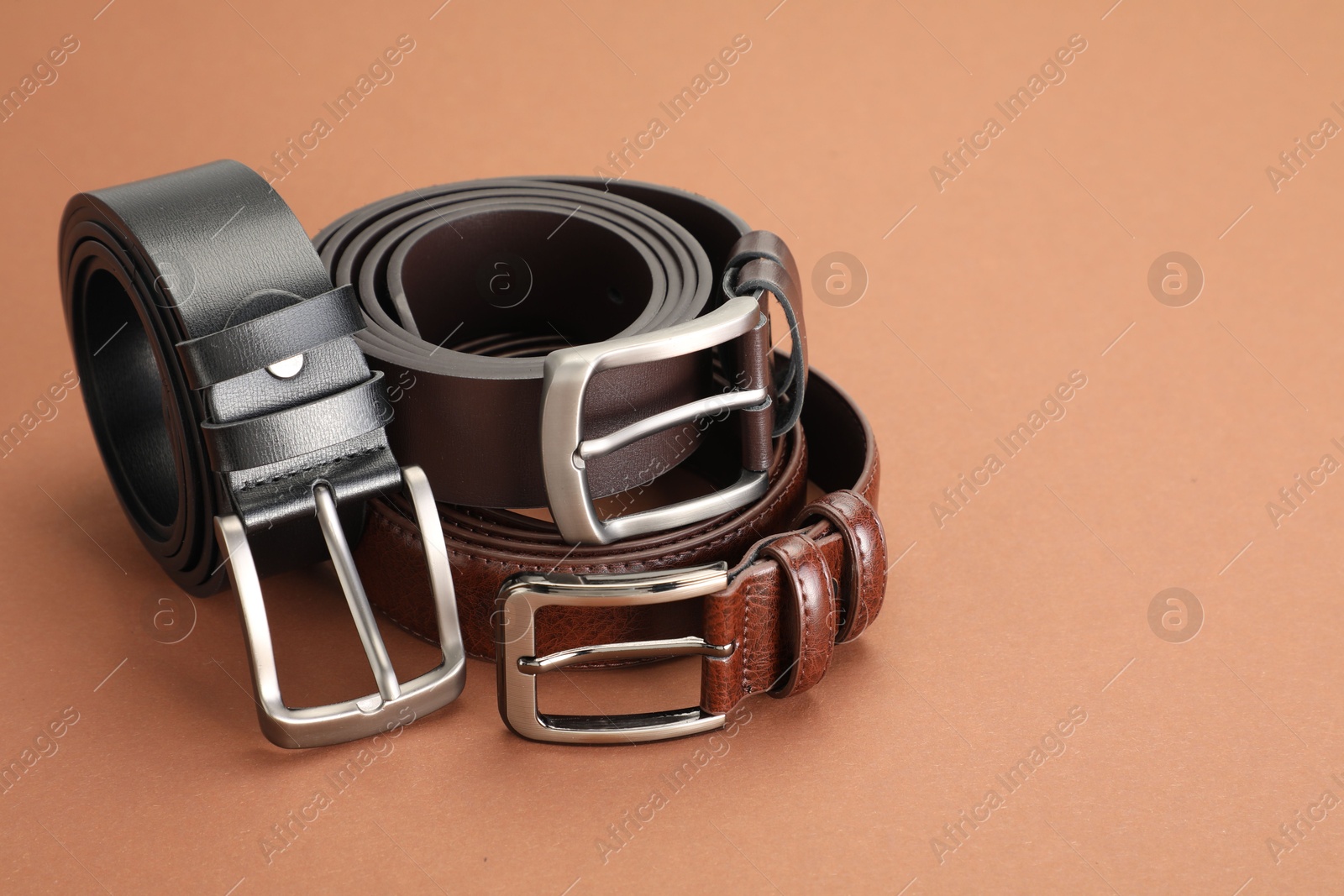 Three leather belts on pale brown background, space for text Photo of Three leather belts on pale brown background, space for text