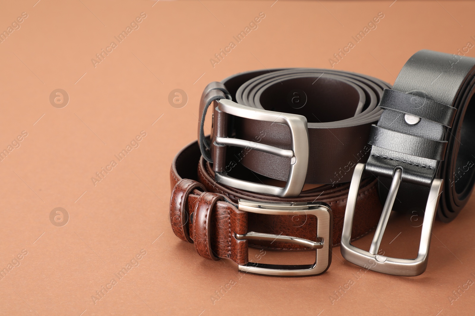 Three leather belts on pale brown background, closeup. Space for text Photo of Three leather belts on pale brown background, closeup. Space for text