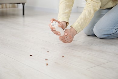 Photo of Young woman spraying insecticide onto cockroaches on floor at home, closeup. Pest problem