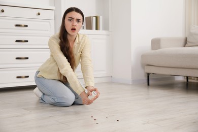 Photo of Emotional young woman spraying insecticide onto cockroaches on floor at home, space for text. Pest problem