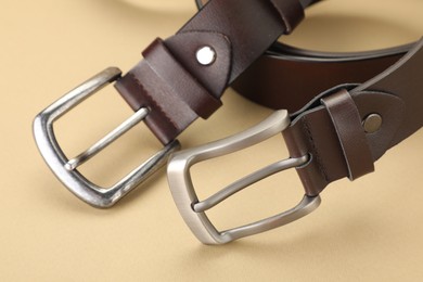 Photo of Two leather belts on beige background, closeup