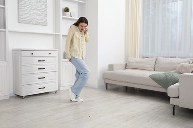 Photo of Emotional young woman looking in disgust at cockroaches on floor indoors. Pest problem