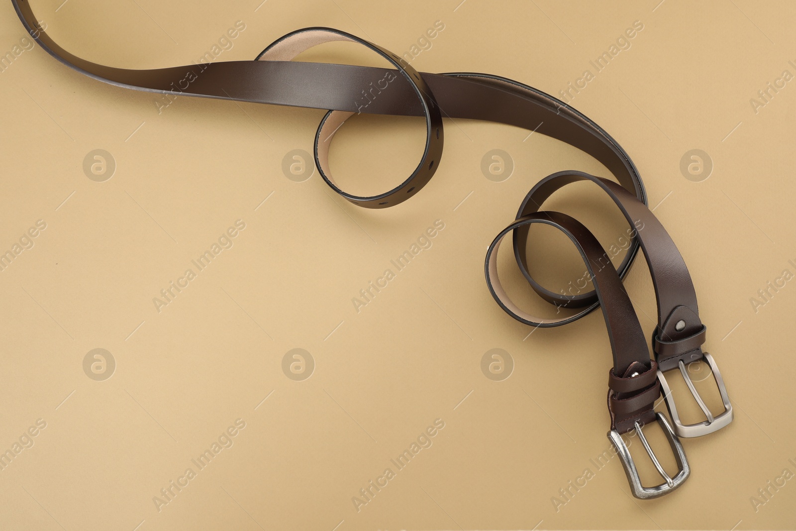 Two leather belts on beige background, flat lay. Space for text Photo of Two leather belts on beige background, flat lay. Space for text