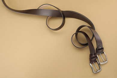 Photo of Two leather belts on beige background, flat lay. Space for text