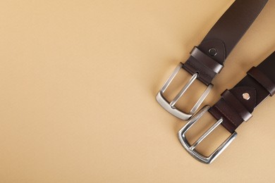 Photo of Two leather belts on beige background, flat lay. Space for text