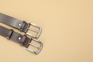 Photo of Two leather belts on beige background, flat lay. Space for text
