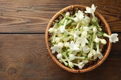 Photo of Wicker bowl with jasmine flowers on wooden table, top view. Space for text