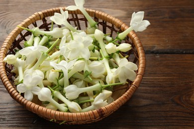 Photo of Wicker bowl with jasmine flowers on wooden table, closeup