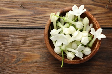 Photo of Bowl with jasmine flowers on wooden table, top view. Space for text