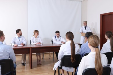 Photo of Senior doctor giving lecture in conference room with projection screen