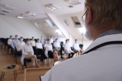 Photo of Senior doctor having discussion with audience in conference room, closeup