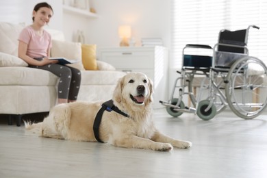 Photo of Girl with disability reading book and her service dog at home, selective focus