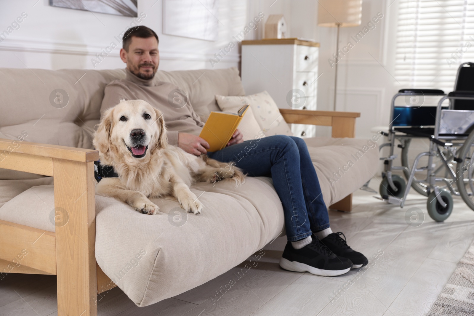 Man with disability reading book and his service dog on sofa at home Photo of Man with disability reading book and his service dog on sofa at home