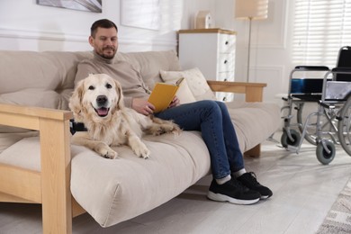 Photo of Man with disability reading book and his service dog on sofa at home