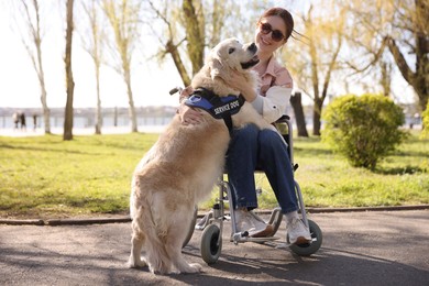 Photo of Woman in wheelchair hugging her service dog at park