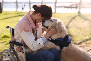 Photo of Woman in wheelchair hugging her service dog at park