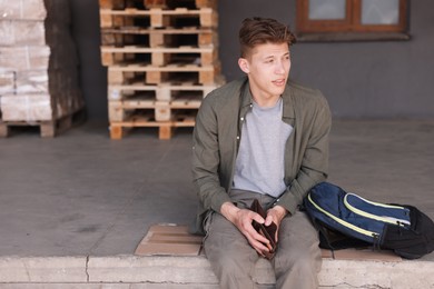 Photo of Man with empty wallet and backpack sitting on concrete floor outdoors. Financial problem