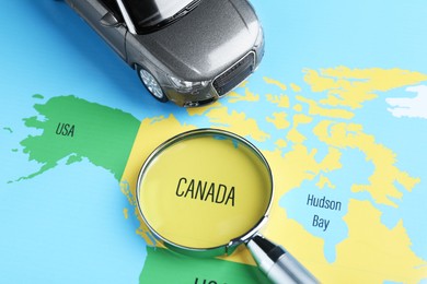 Photo of Road trip concept. Toy car and magnifying glass on world map, above view
