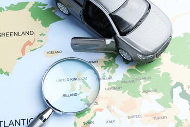 Photo of Road trip concept. Toy car and magnifying glass on world map, above view