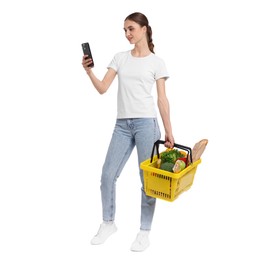 Photo of Woman with shopping basket full of products and smartphone on white background