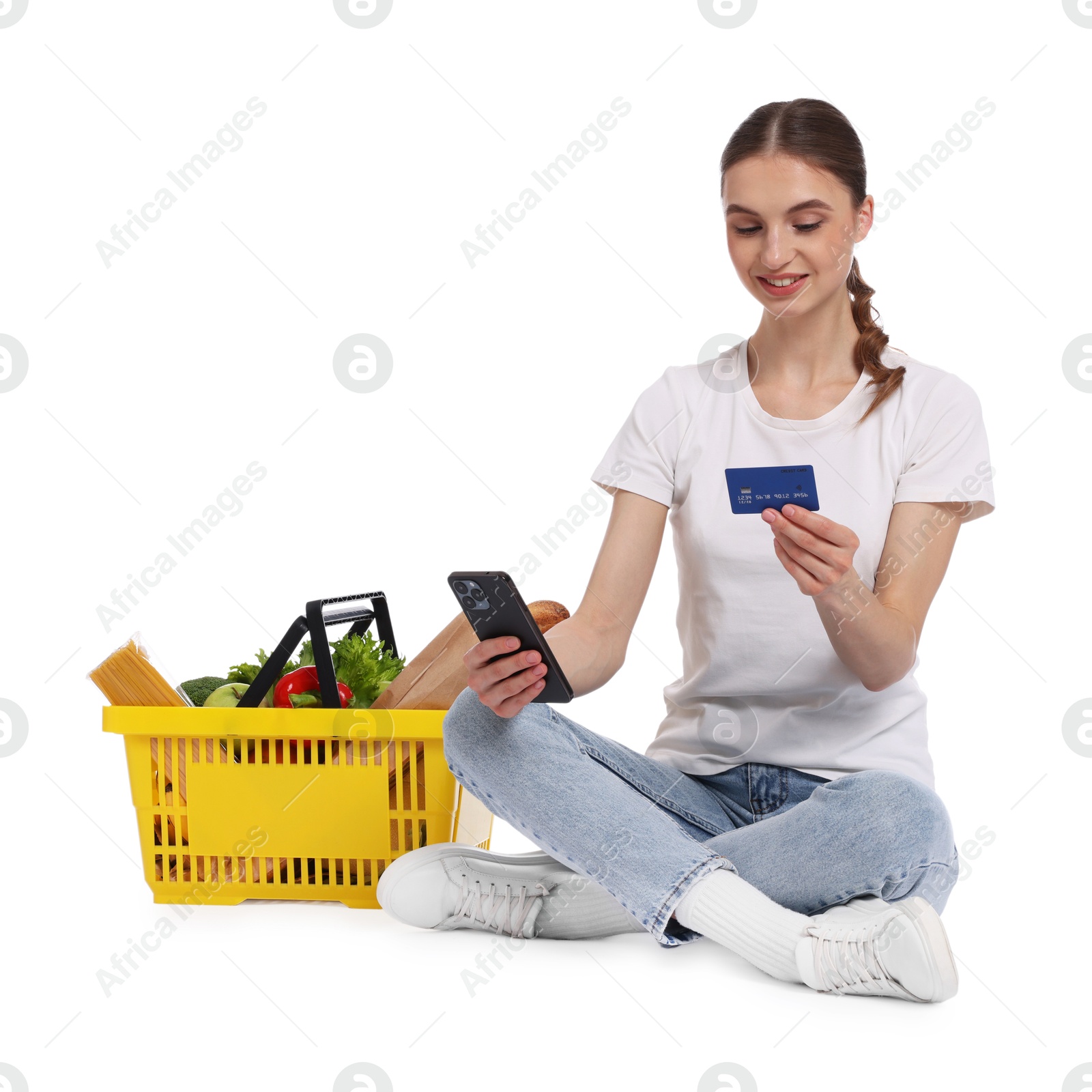 Photo of Woman with shopping basket full of products, credit card and smartphone on white background