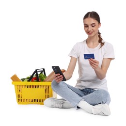 Photo of Woman with shopping basket full of products, credit card and smartphone on white background