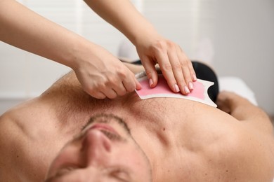 Photo of Young man undergoing wax epilation in salon, closeup