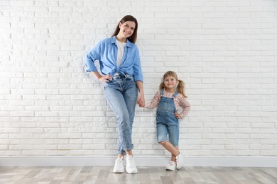 Photo of Beautiful mother and her little daughter near white brick wall