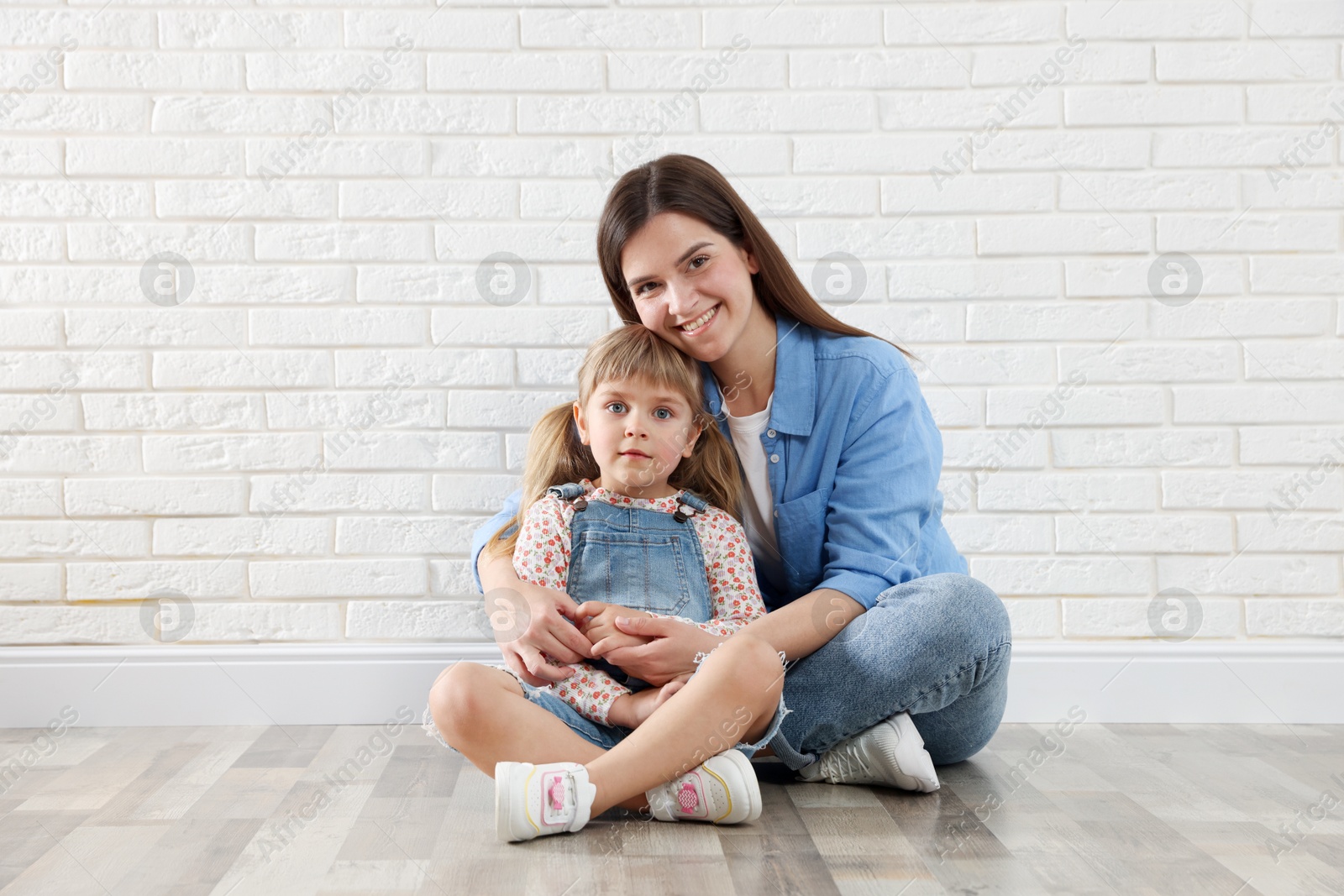 Photo of Beautiful mother and her little daughter near white brick wall