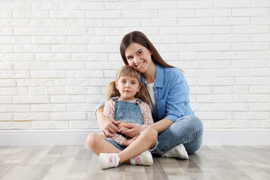 Photo of Beautiful mother and her little daughter near white brick wall