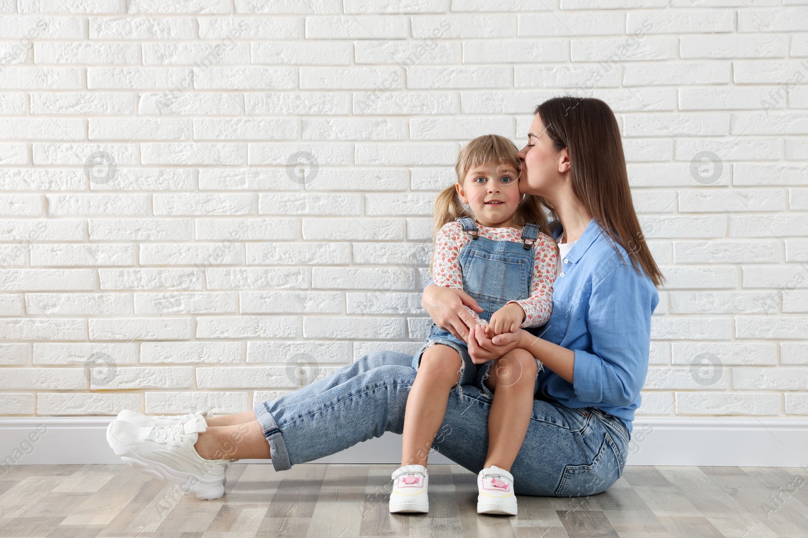 Photo of Beautiful mother and her little daughter near white brick wall. Space for text