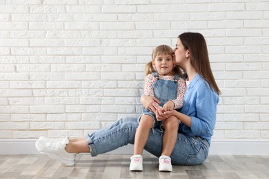 Photo of Beautiful mother and her little daughter near white brick wall. Space for text
