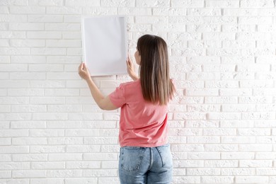Photo of Woman hanging blank frame on white brick wall, back view