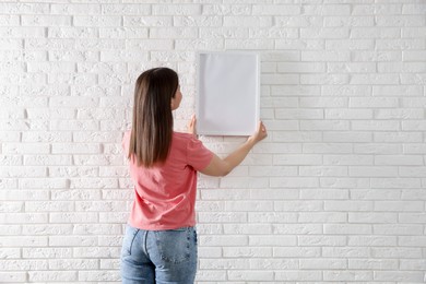 Photo of Woman hanging blank frame on white brick wall, back view