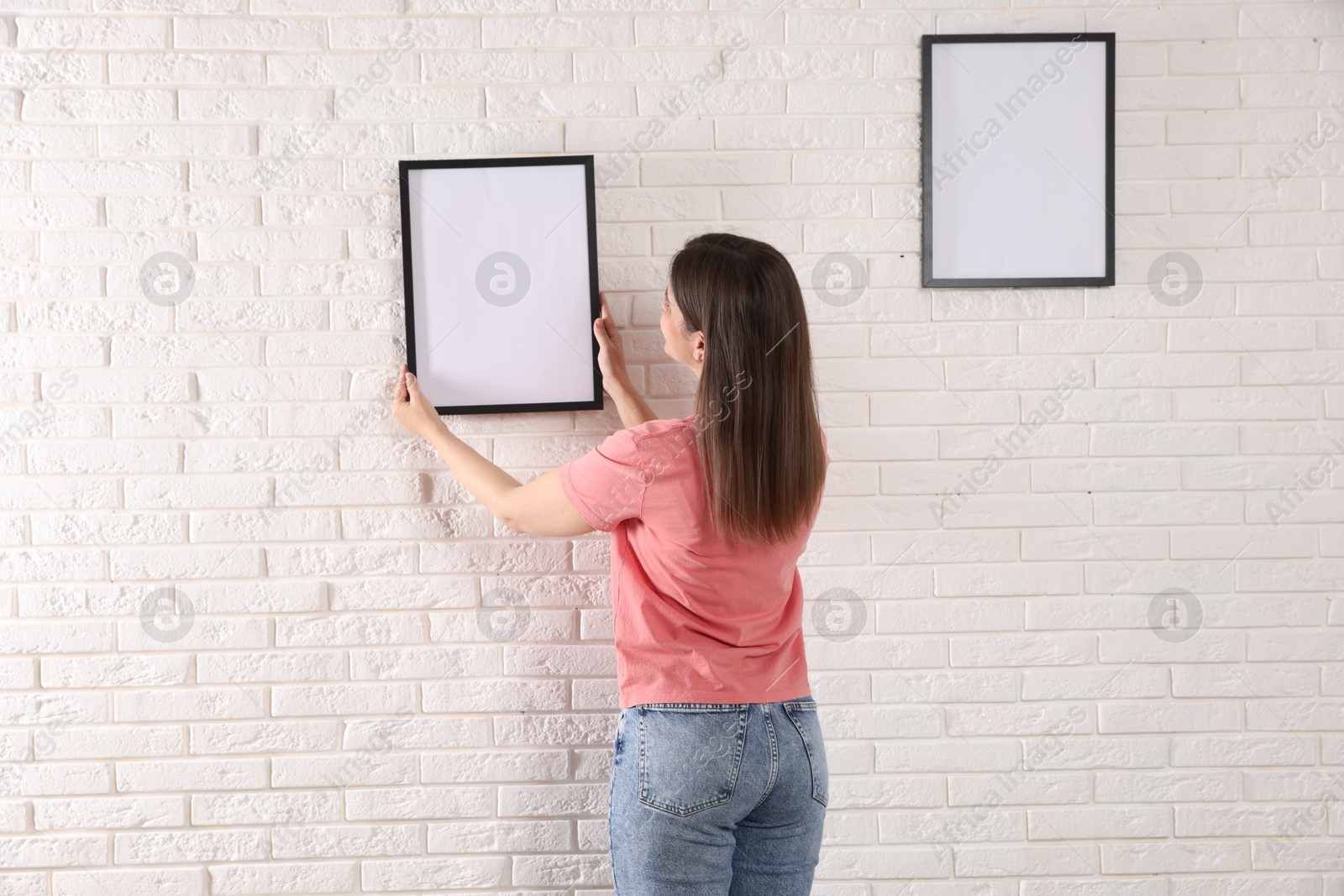 Photo of Woman hanging blank frames on white brick wall, back view