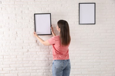 Photo of Woman hanging blank frames on white brick wall, back view