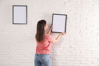 Photo of Woman hanging blank frames on white brick wall, back view