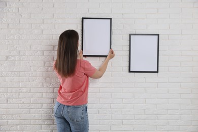 Photo of Woman hanging blank frames on white brick wall, back view