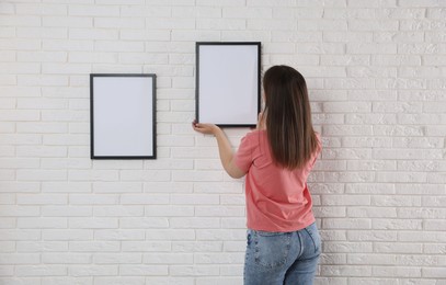Photo of Woman hanging blank frames on white brick wall, back view