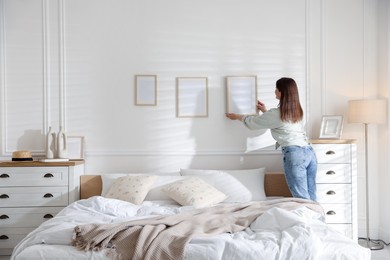 Photo of Woman hanging blank frames on white wall in bedroom
