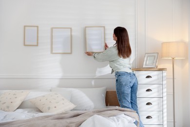 Photo of Woman hanging blank frames on white wall in bedroom