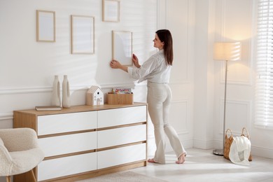Photo of Woman hanging blank frames on white wall indoors
