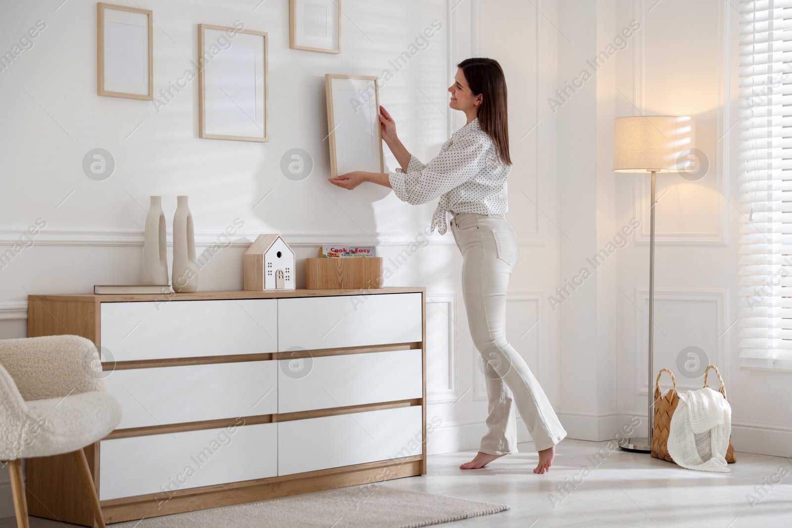 Photo of Woman hanging blank frames on white wall indoors