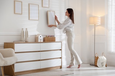 Photo of Woman hanging blank frames on white wall indoors
